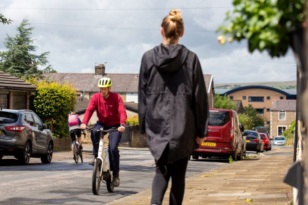 A woman walking on a pavement, two people cycling on the road